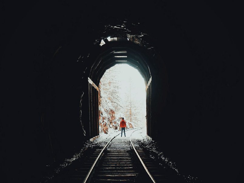 A person standing on the tracks in front of an open tunnel.