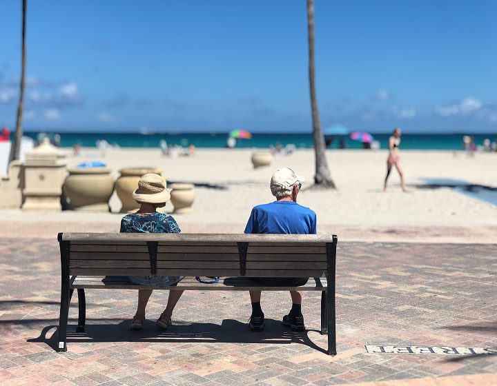 Two people sitting on a bench near the beach.