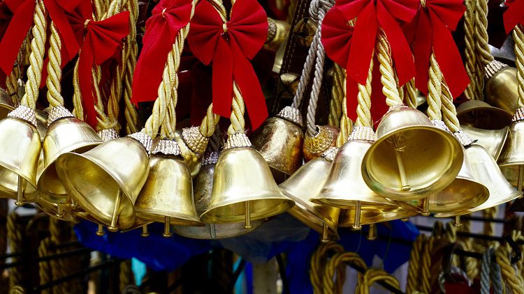 A group of bells hanging from ropes with red bows.