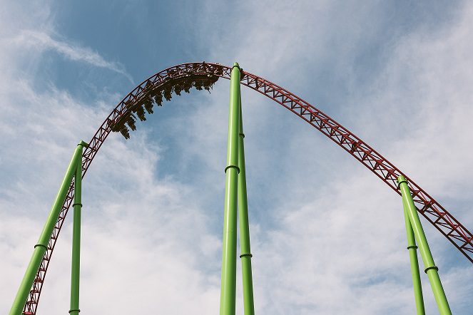 A green roller coaster with people riding it.