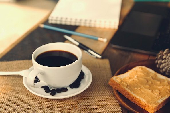 A cup of coffee on a saucer next to some toast.