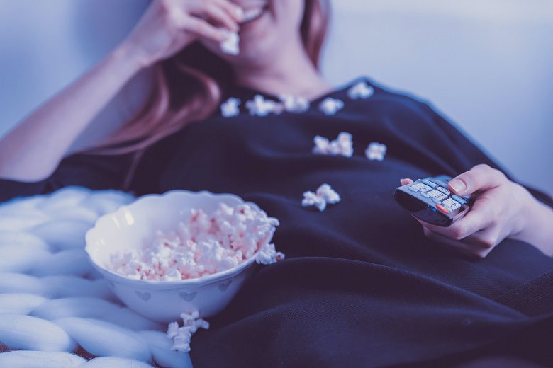 A woman is eating popcorn while sitting on the bed.