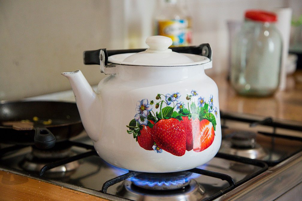A tea pot with strawberries on it sitting on the stove.
