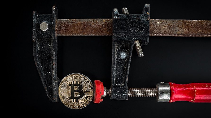 A metal clamp holding a bitcoin in it's vise.